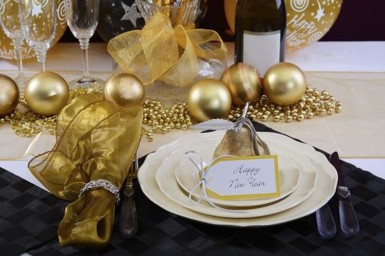 Happy New Years Eve elegant dinner table setting with black and gold decorations, balloons and stylish centerpiece, close up.