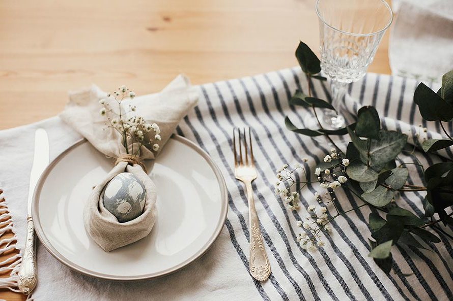 Easter brunch table setting with egg in easter bunny napkin. Modern natural dyed blue egg on napkin with bunny ears, flowers on plate and vintage cutlery. Easter table decorations