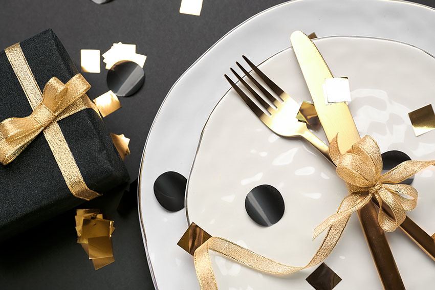 Gold cutlery tied with beautiful ribbon on plate, closeup