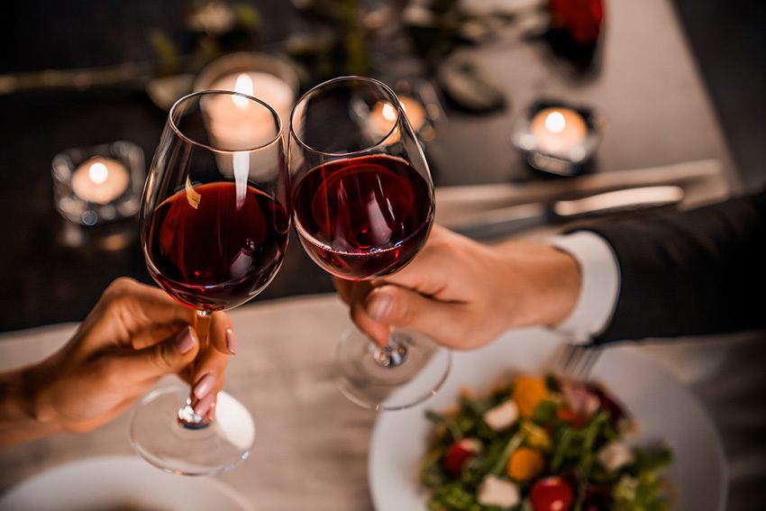 Close up of young couple toasting with glasses of red wine at restaurant on Valentine's Day